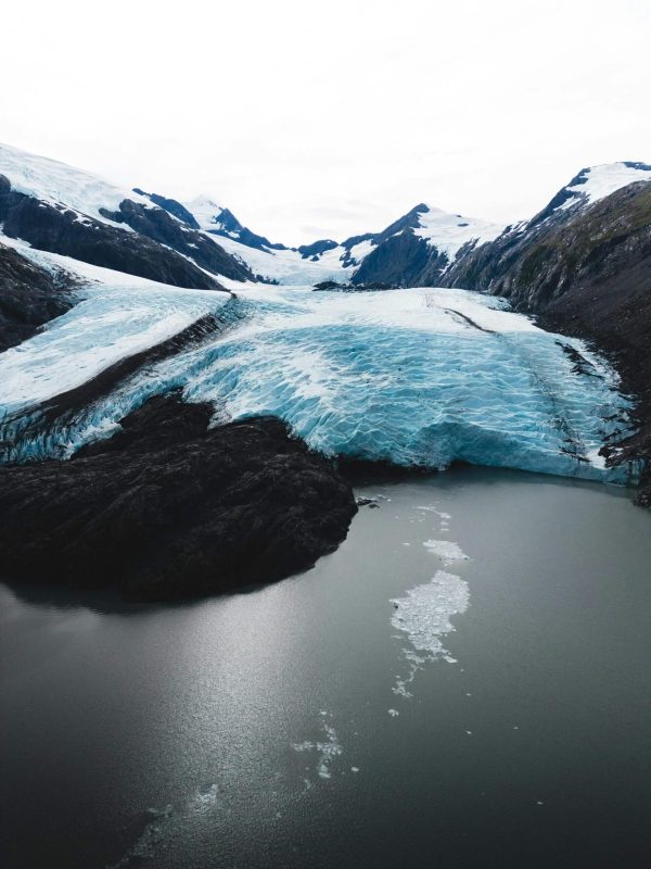 A glacier melting into a lake surrounded by snowy mountains.